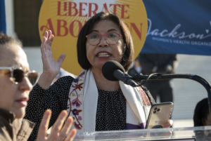 Rabbi Mira Rivera, Rabbi and Board Certified Chaplain at Romemu speaks at a podium at the Abortion is Essential Rally in front of the U.S. Supreme Court.